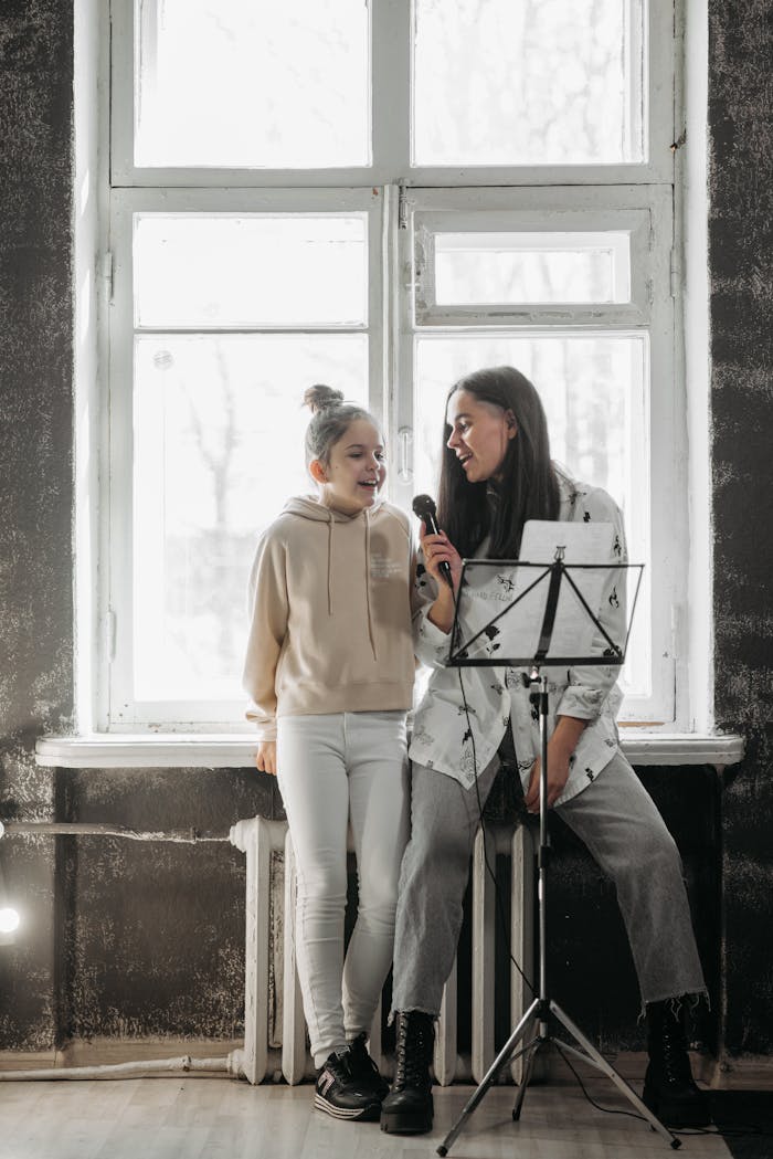 A mother and daughter engage in a joyful singing lesson together by a bright window.